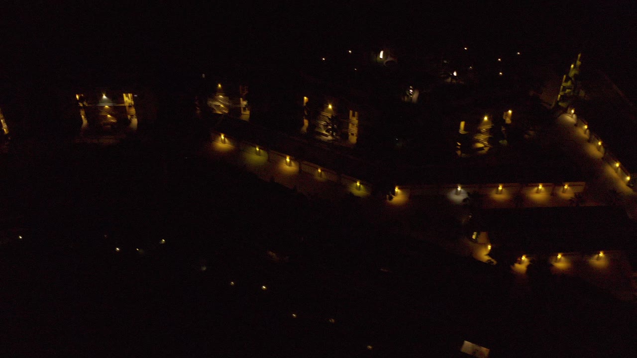 Dark overhead night view with scattered warm lights and shadowed structures.