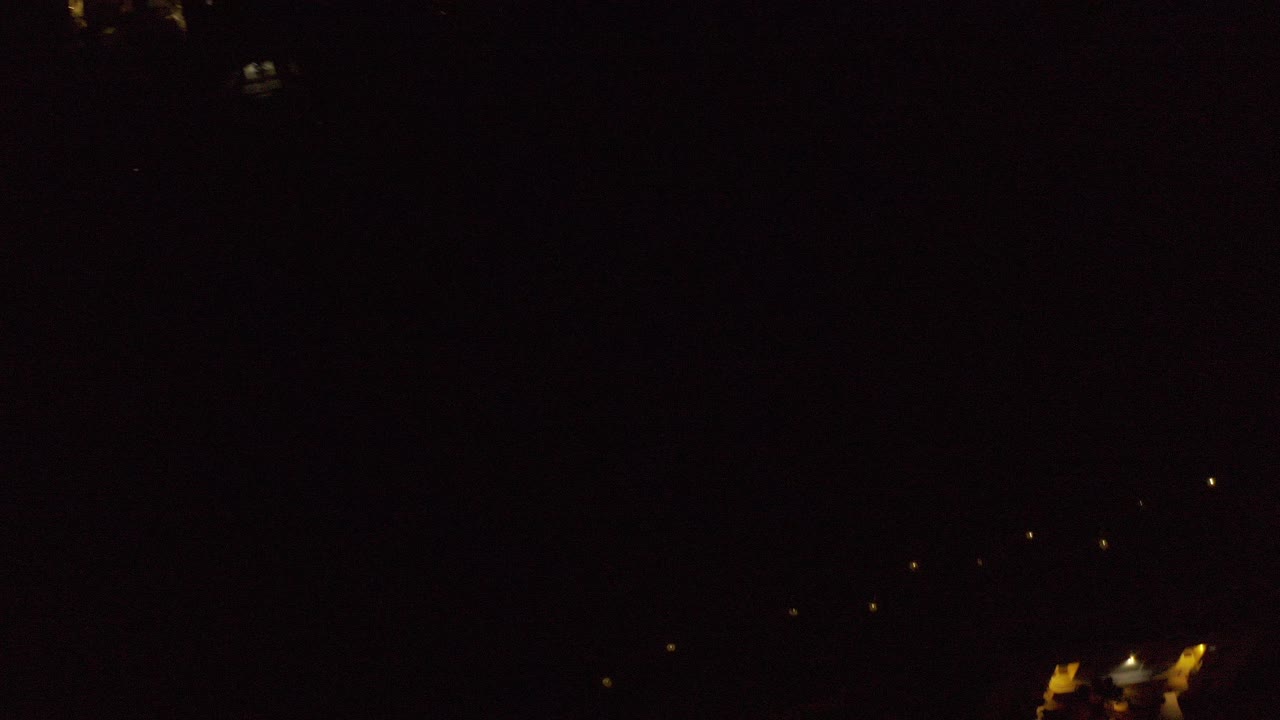 Dark aerial view with scattered warm lights and faint rooftops.