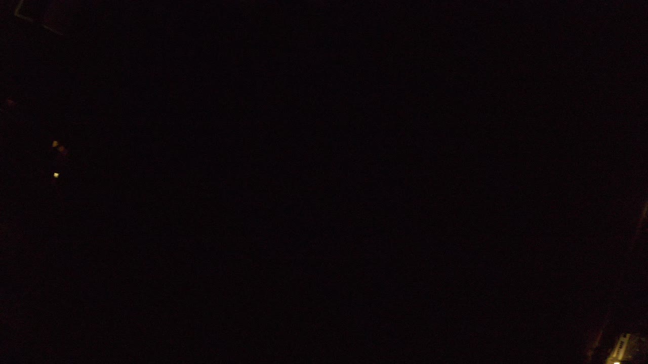 Very dark aerial view with faint streetlights and rooftops.