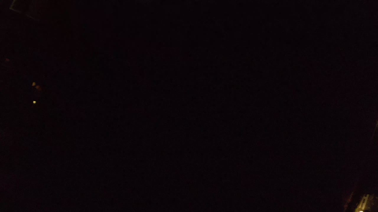 Second frame over Los Cabos at night, showing a dim diagonal road edge, scattered building lights, and heavy shadow, no visible people.