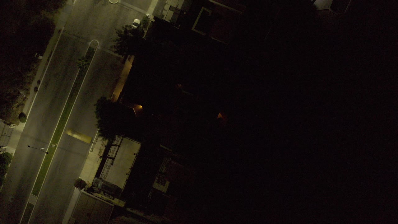 Overhead night view of a lit road beside dark buildings.