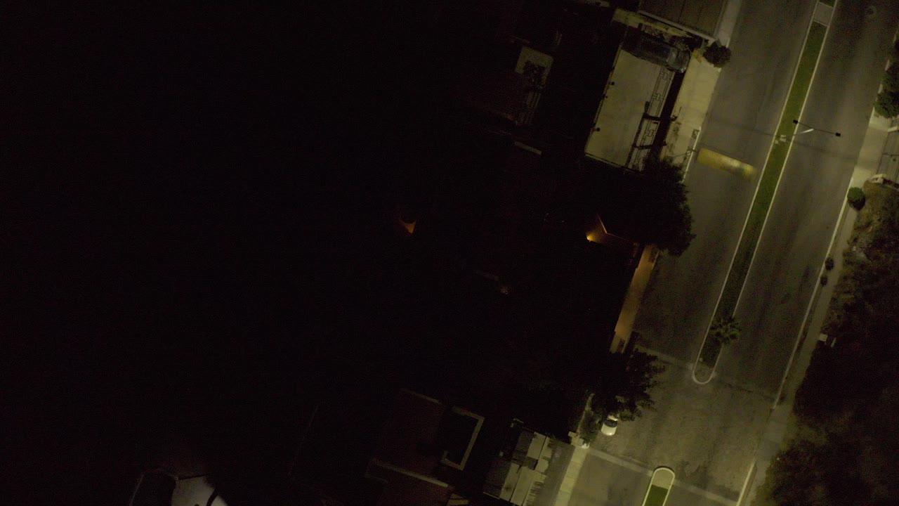 Overhead nighttime road with street lamps and dark buildings.