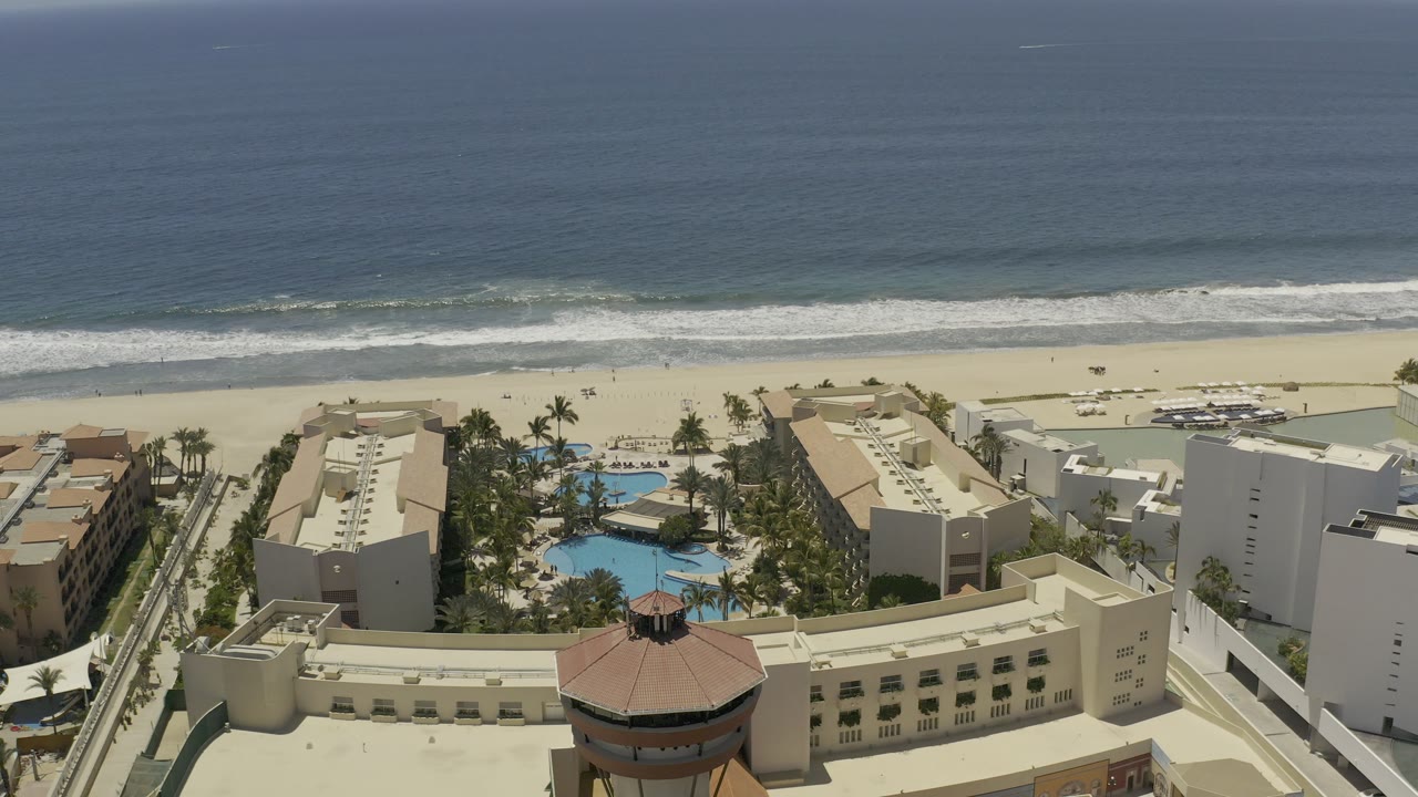 Aerial view of resort buildings, pools, beach, and ocean surf.