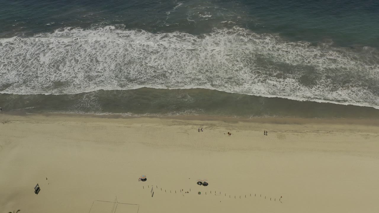 High view of waves washing toward an open sandy beach.