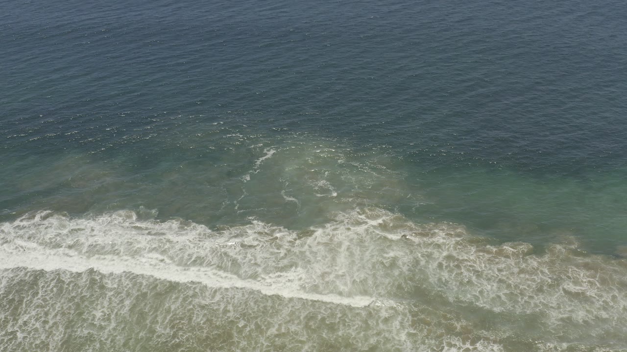 Elevated view of blue-green ocean water in Los Cabos, Mexico, with white surf breaking across the lower part of the frame and no visible people.