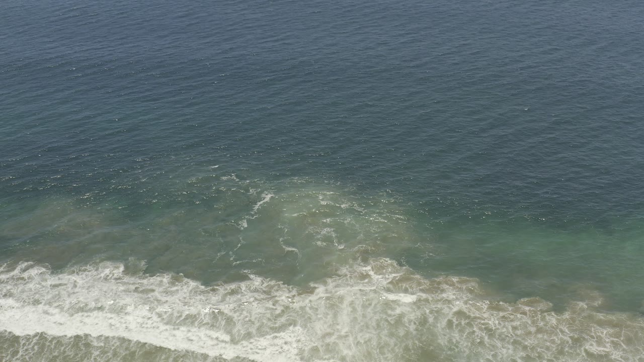 Los Cabos, Mexico ocean overview with foamy white breakers crossing the lower frame and darker blue water beyond, with no visible people.