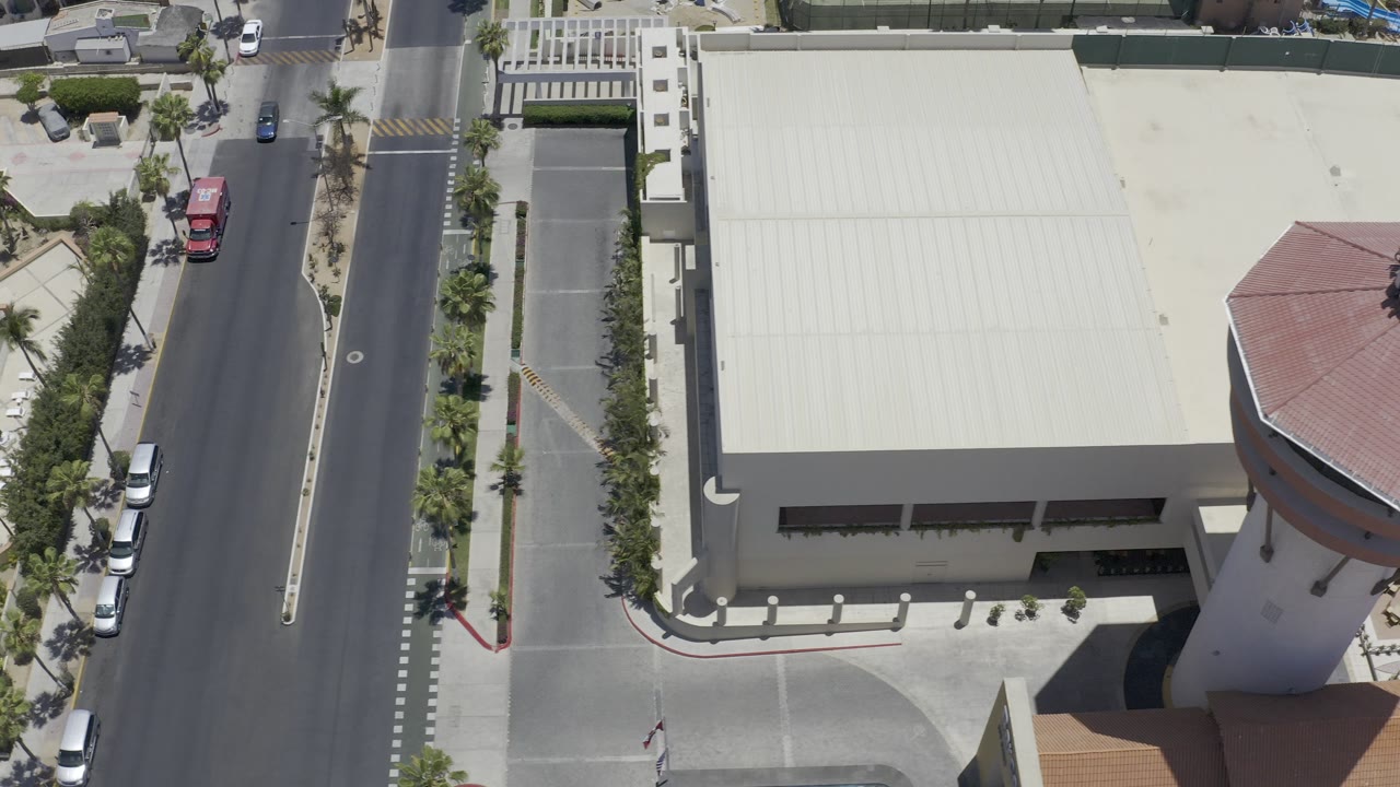 Overhead view of a road beside a large pale-roofed building and palm landscaping.