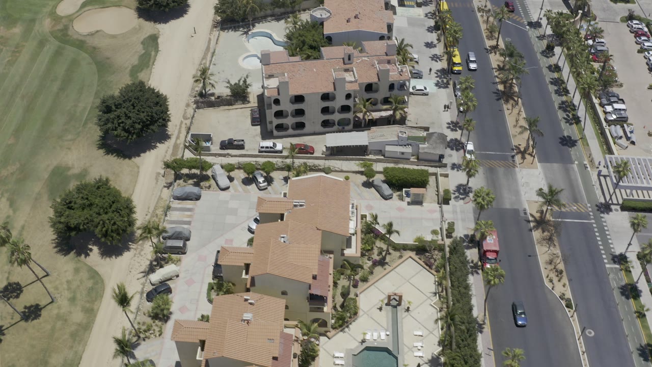Aerial view of condos, road, parked cars, and green grounds.