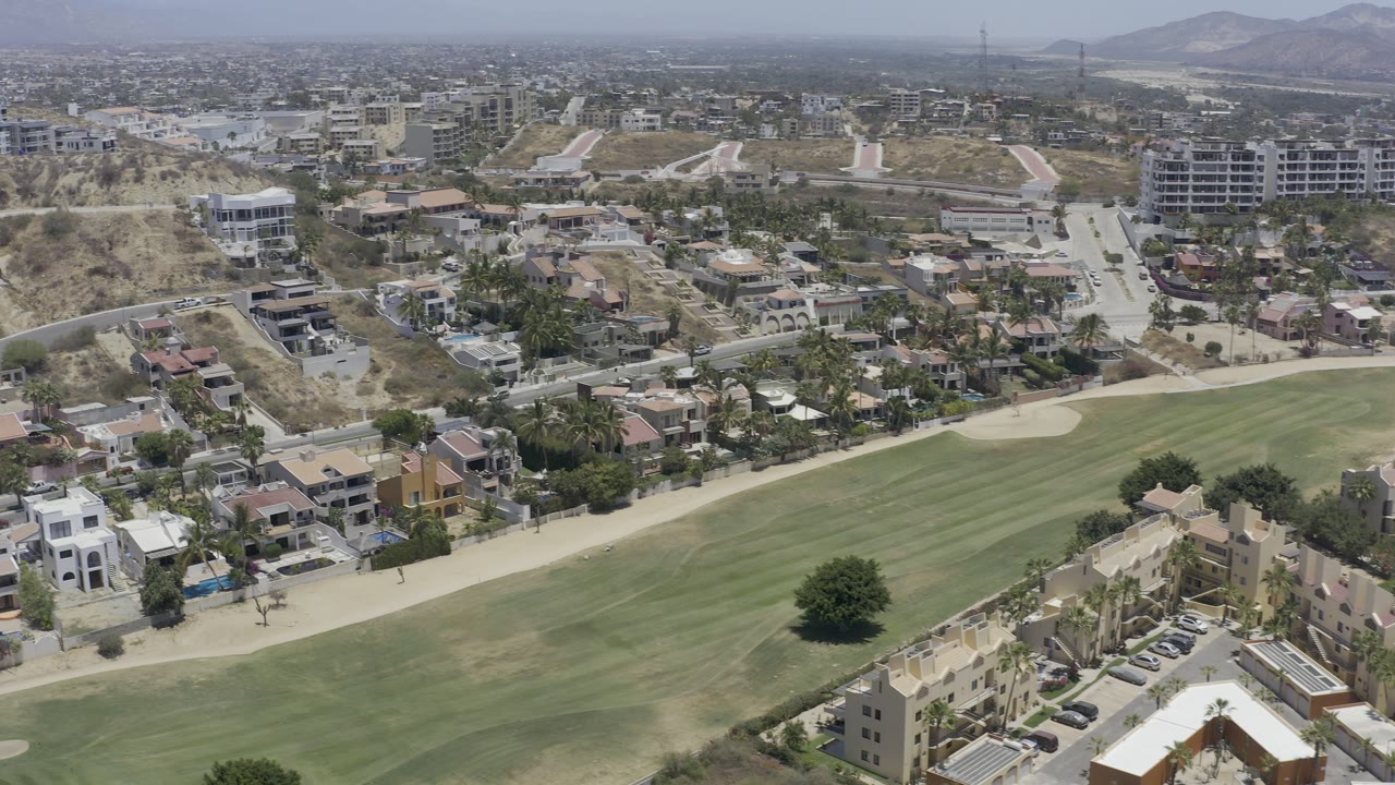 Aerial view of green fairway, hillside homes, roads, and distant town buildings.