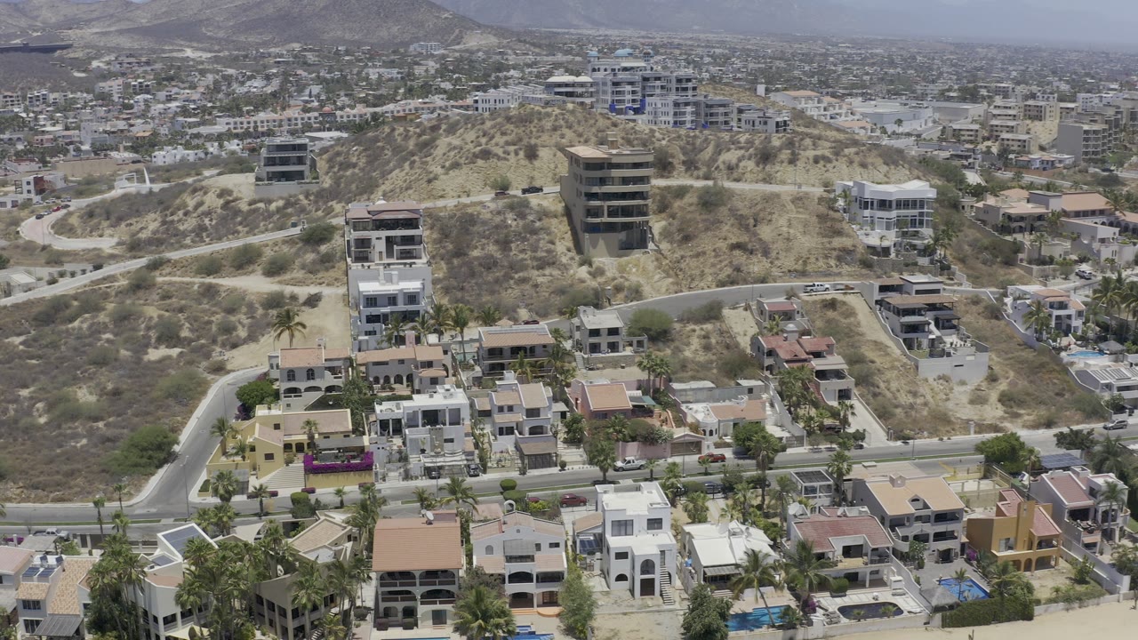Aerial view of hillside homes, roads, dry slopes, and distant buildings.