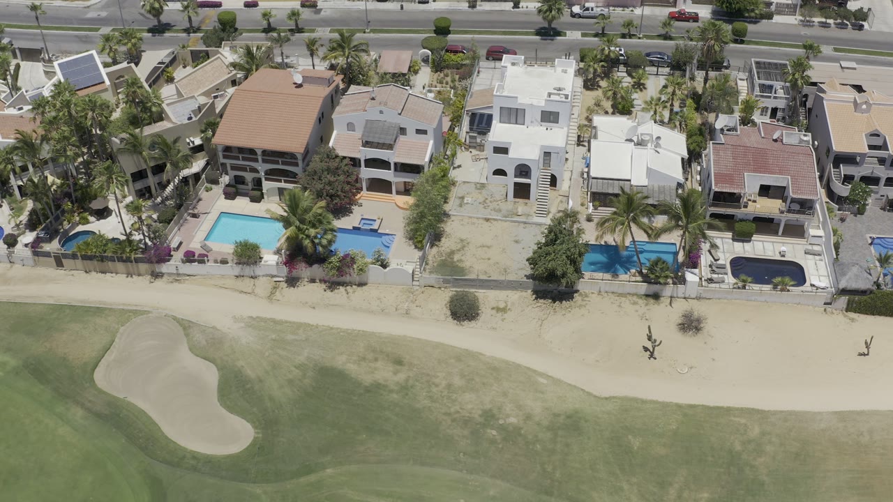 Aerial view of beachfront villas with pools beside sand and turf.