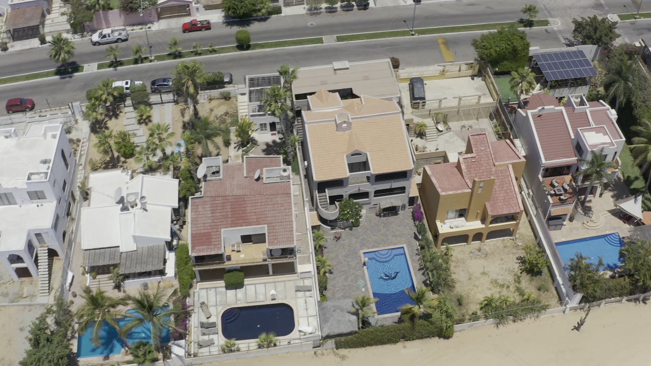 Overhead view of homes, pools, a road, and parked cars.