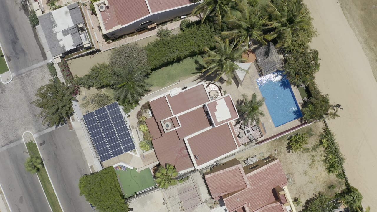 Overhead view of coastal houses, pool, palms, road, sand, and solar panels.