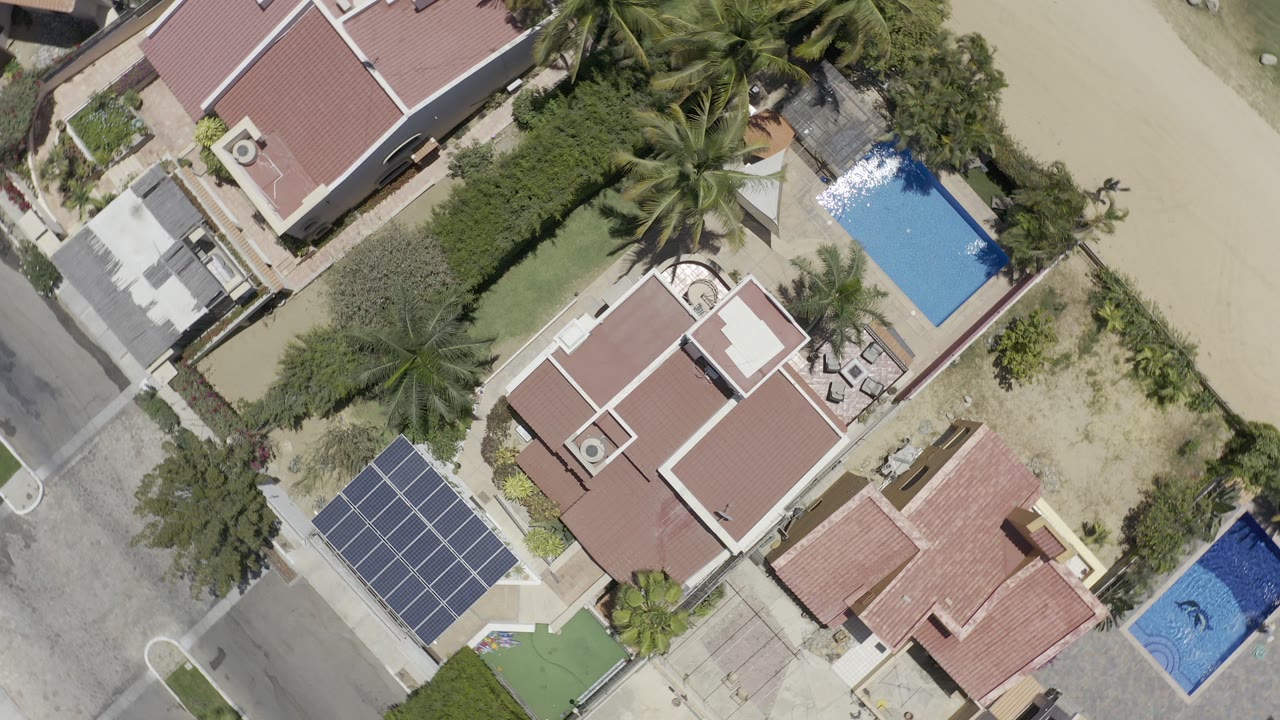 Overhead view of red-roofed homes, a pool, palms, road, and solar panels.