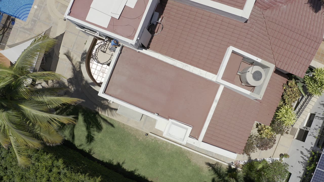 Overhead view of red tile roof, lawn, palms, walkway, and pool edge.