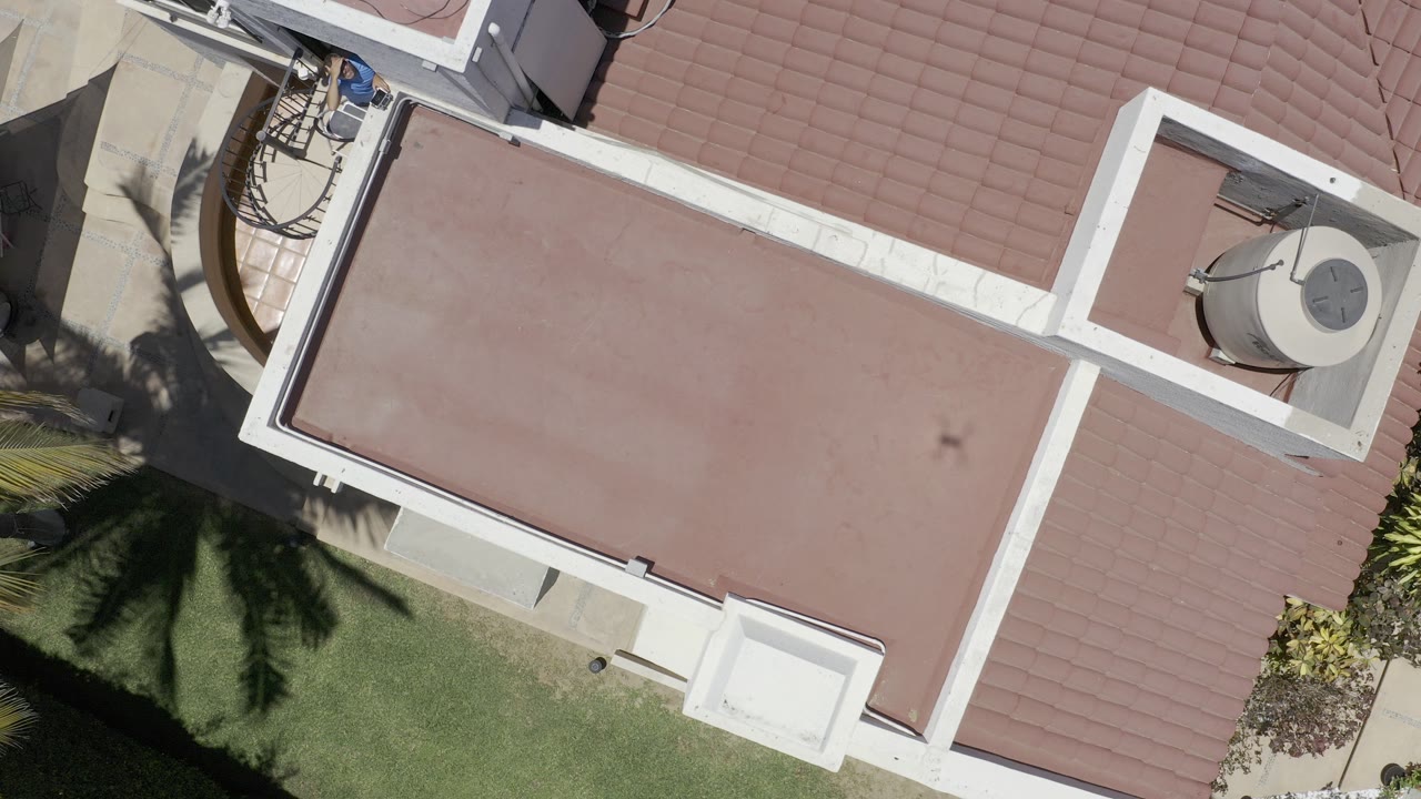Top-down view of a red flat roof beside palm shadows and grass.