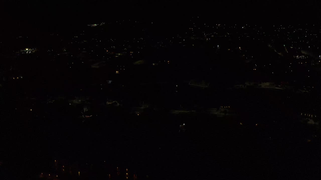 A dark Los Cabos, Mexico city-light view one second in, with small white and amber points of light and no visible people.