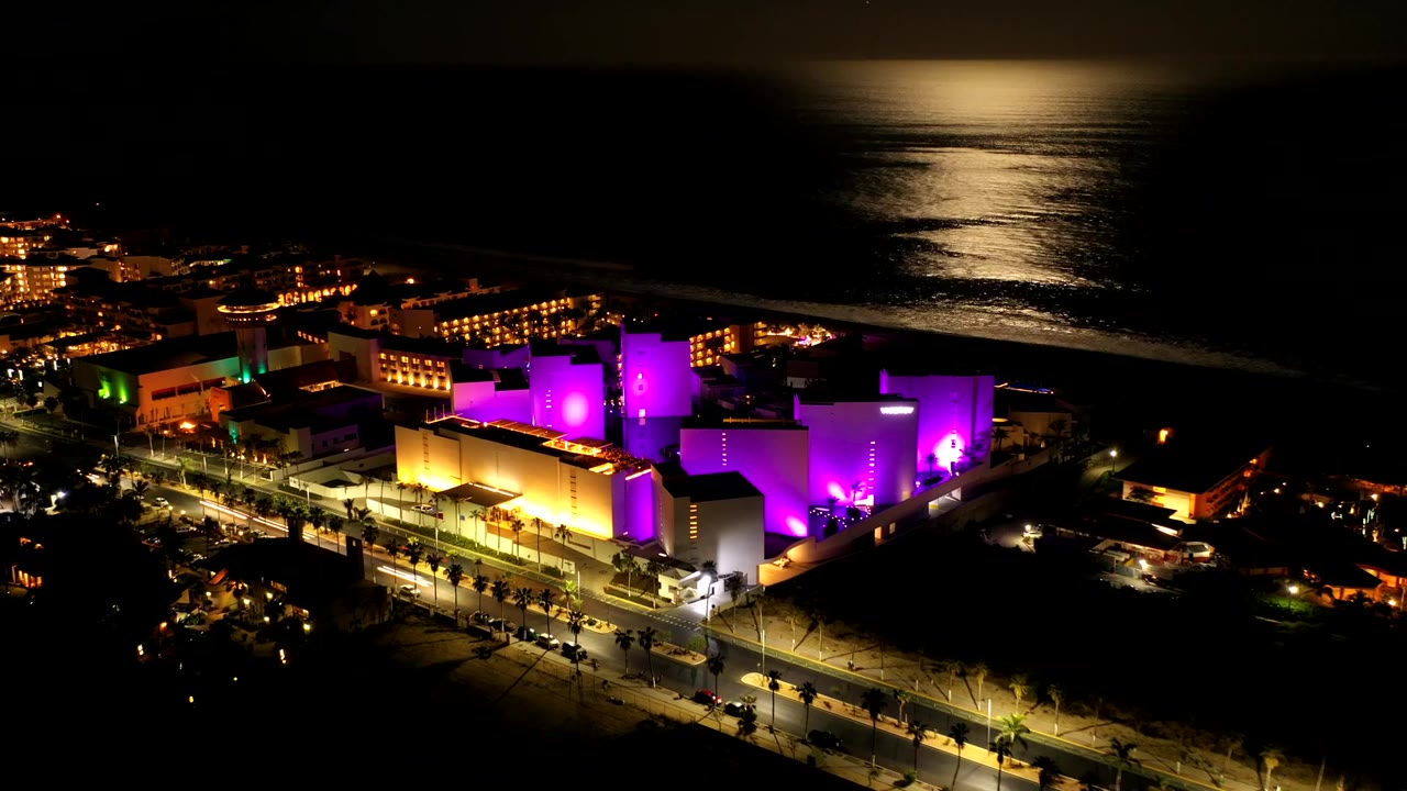 Colorful waterfront buildings at night with roads and ocean behind them.