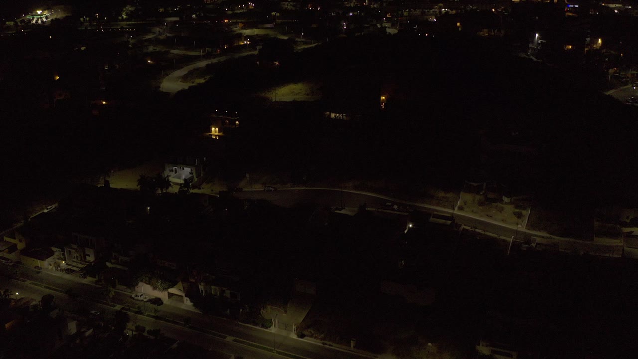 Dark aerial view of roads, houses, and scattered city lights at night.