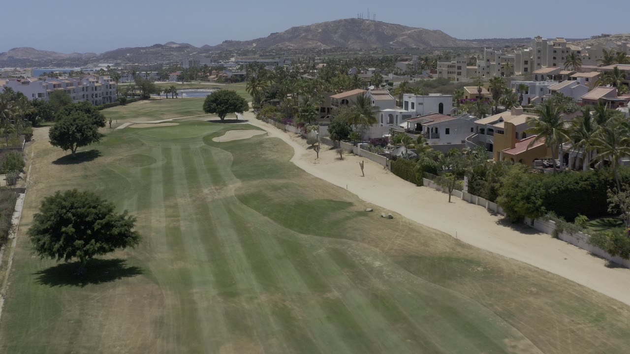 Aerial view of a golf fairway beside homes and hills.