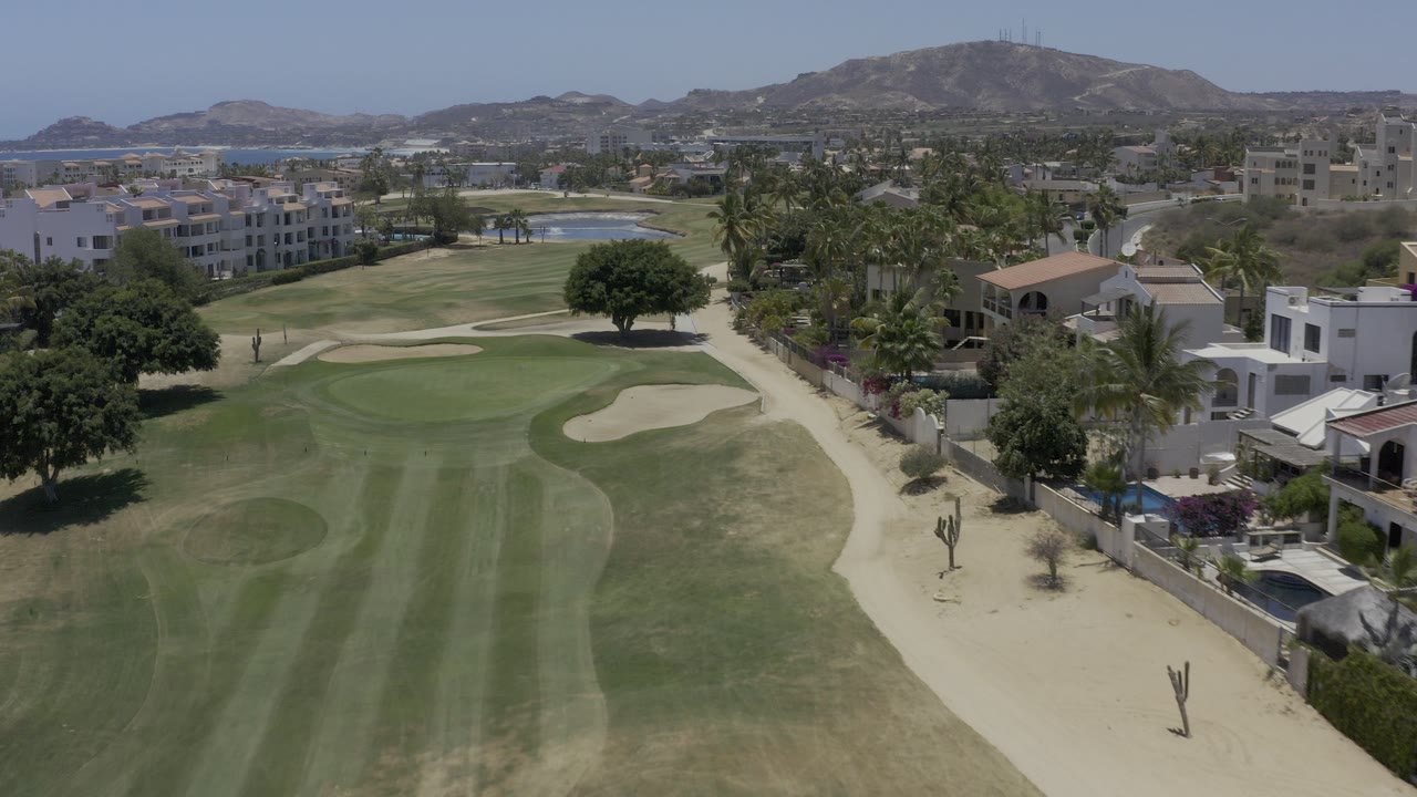 Aerial view of golf fairway, sand bunkers, palms, buildings, hills, and distant water.