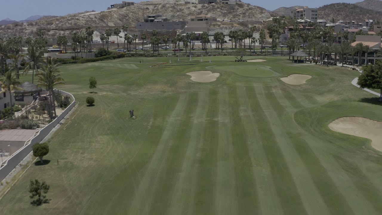 Elevated view over a striped green fairway with sand bunkers and rocky hills beyond.