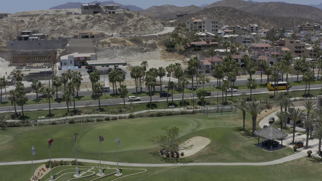 Aerial view of golf green, palm-lined road, hillside homes, and dry hills.
