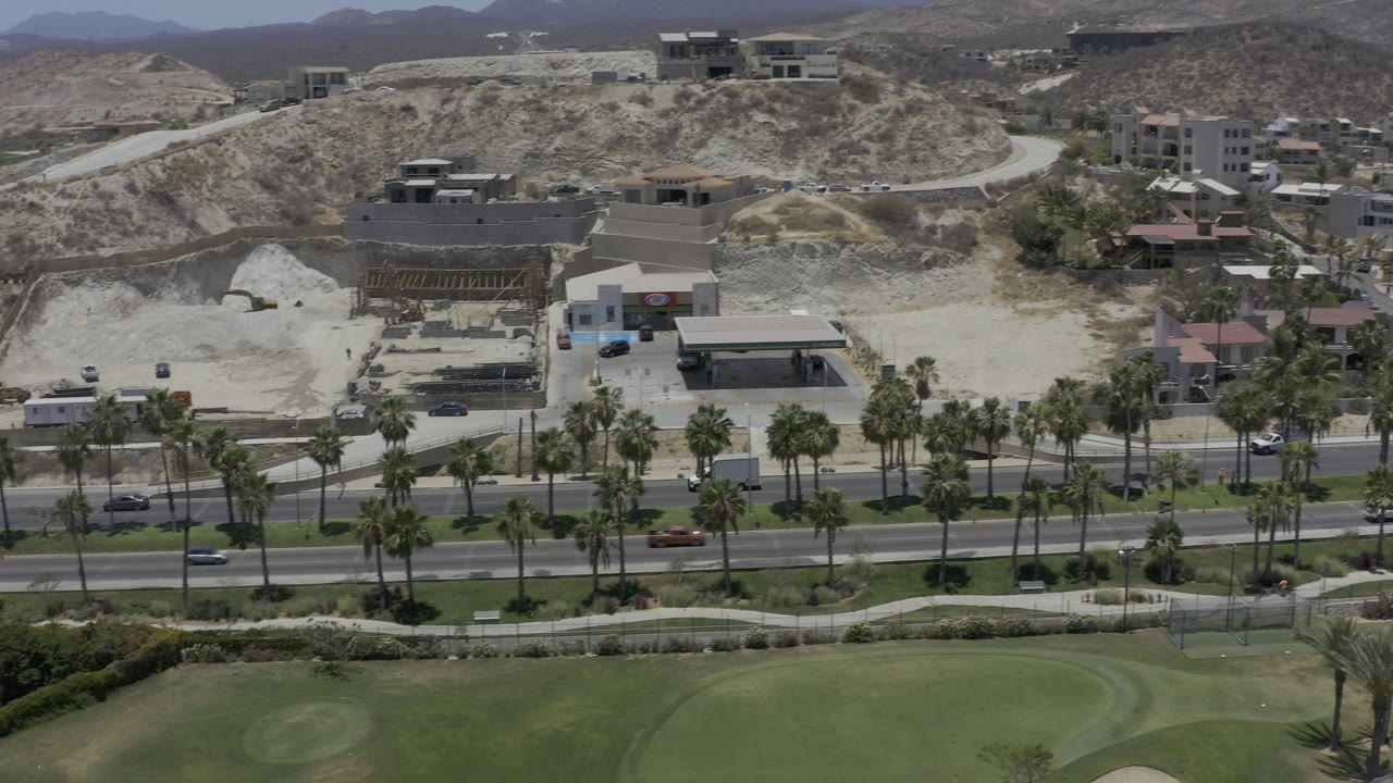 Aerial view of a palm-lined road, green lawn, buildings, and dry hills.