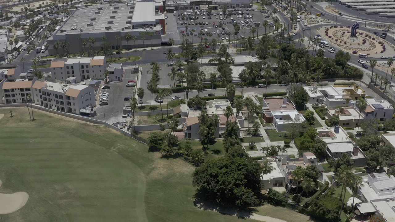 Aerial view over green course land, homes, trees, roads, and parking lots.