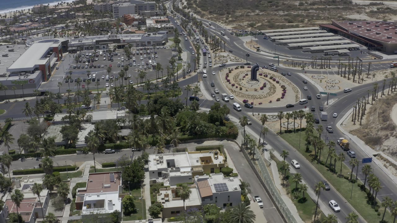 Aerial view of a roundabout, roads, parking lot, homes, and dry open land.