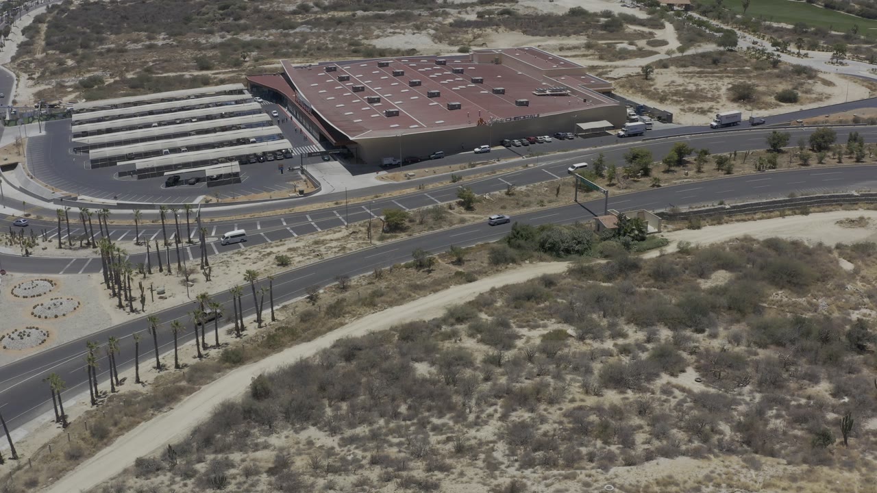 Drone-like aerial view of a red-roofed building beside roads and scrubland.