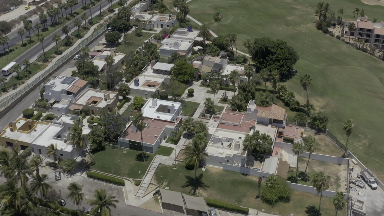 Aerial view of homes beside a golf course and palm-lined roads.