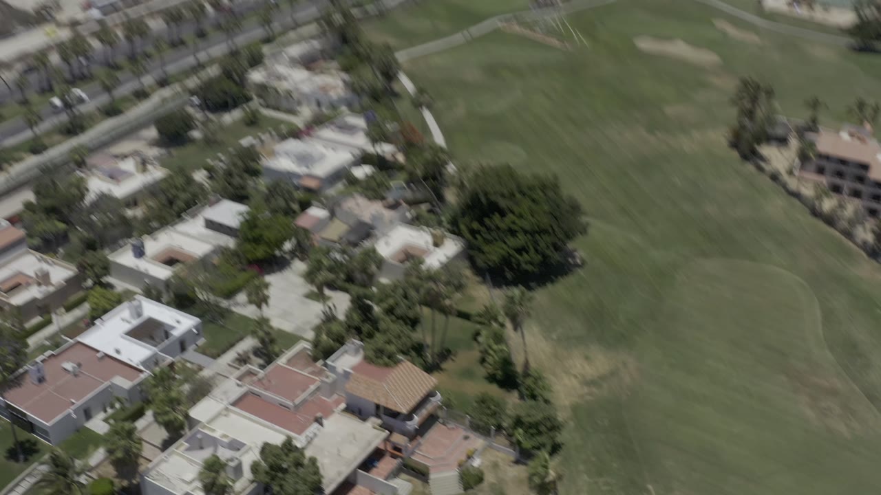 Aerial view in Los Cabos showing fairways and sand bunkers bordered by homes, resort buildings, roads, palms, and no visible people.