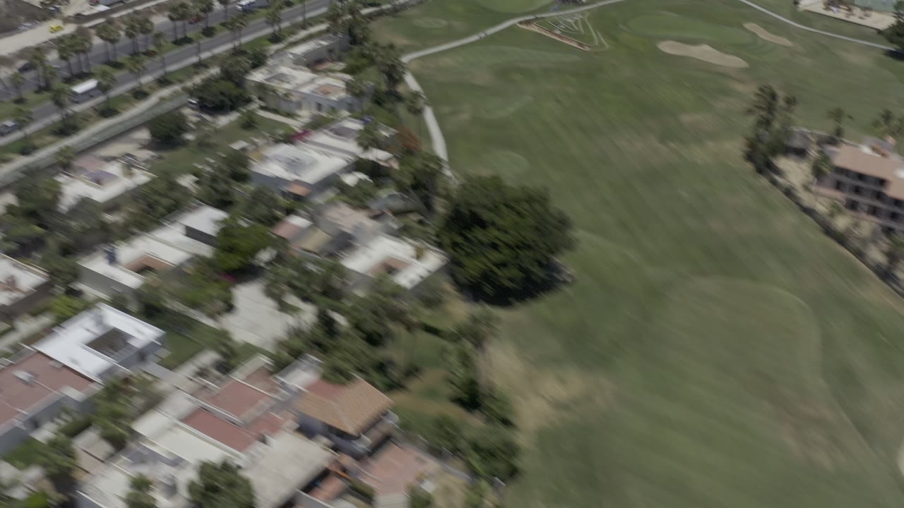 Aerial view of a golf course beside resort buildings and palms.