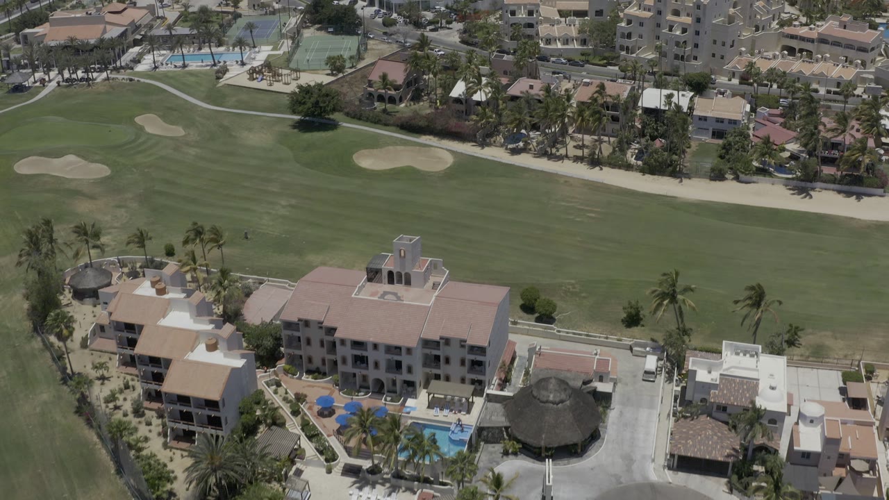 Aerial view of golf course, palm trees, pools, and residential buildings.