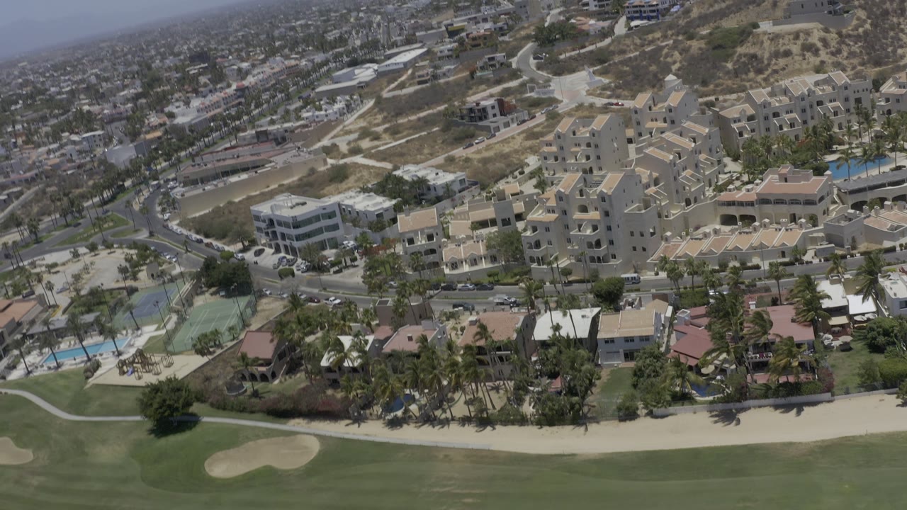 Aerial view of golf course fairway below hillside apartments and homes.