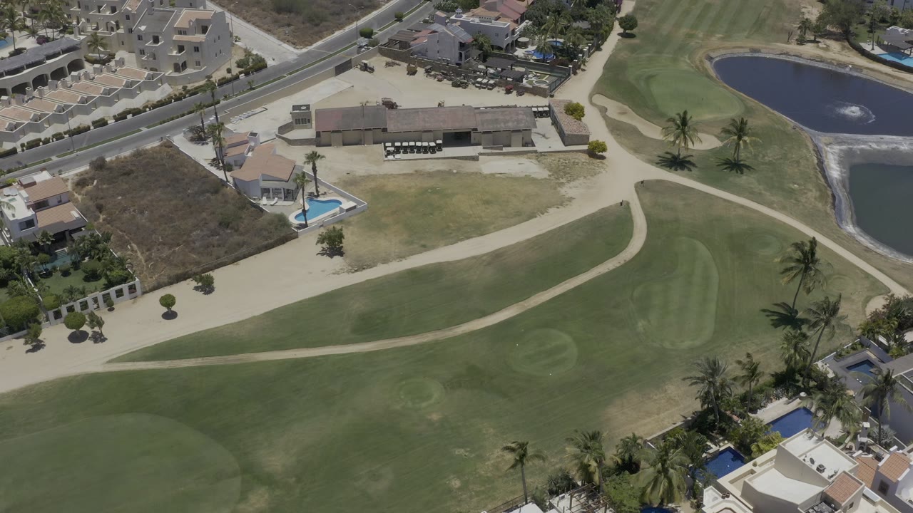 Overhead golf course with fairways, cart path, villas, road, palms, and water feature
