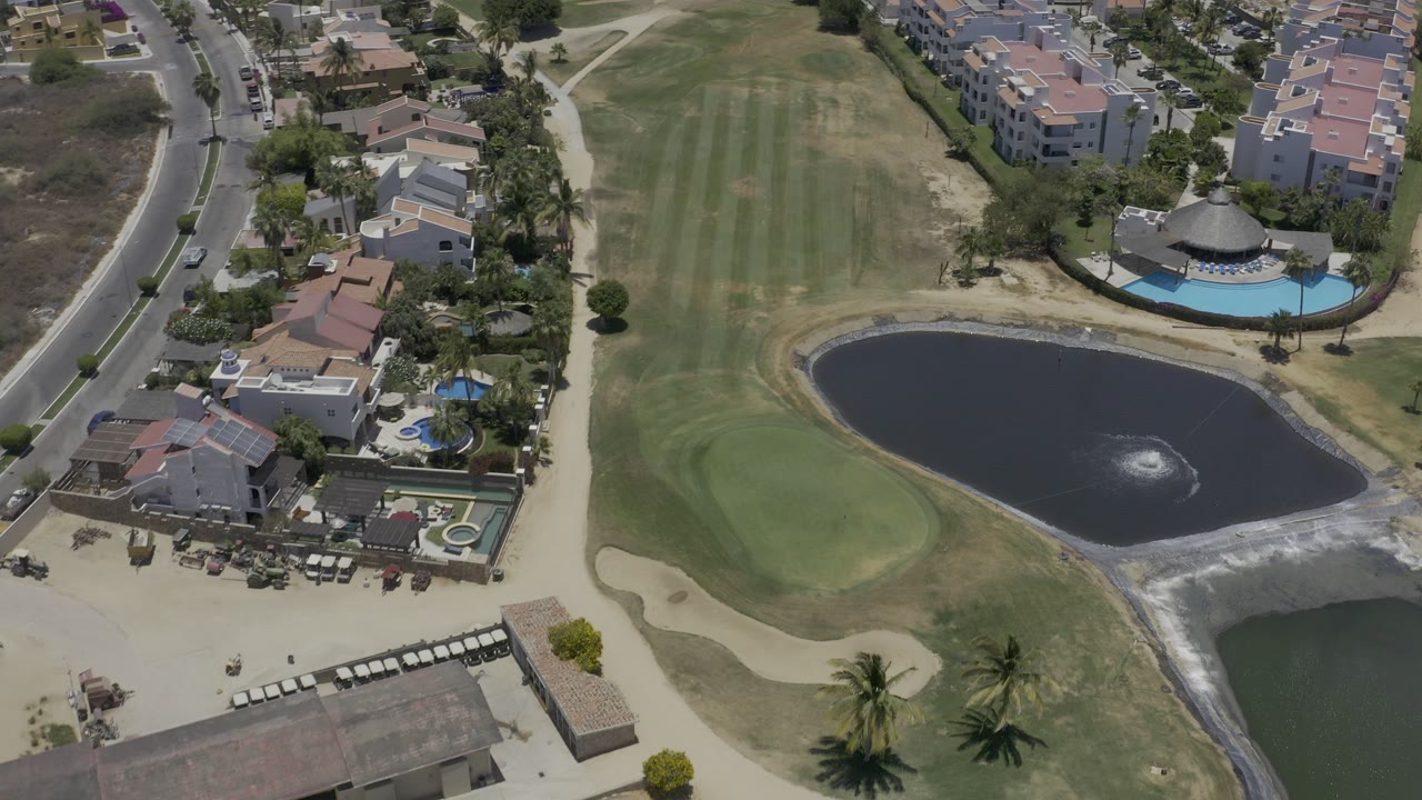 Aerial view of a golf course pond, fairway, homes, and pool area.