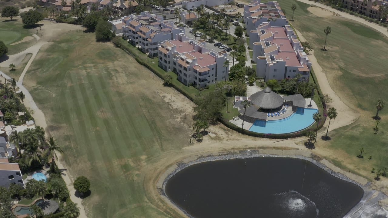Residential buildings and pool beside grass, paths, palms, and pond.