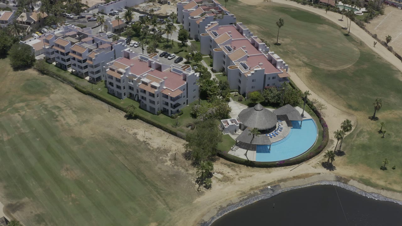Aerial view of condo buildings, lawns, pool, and pond edge.