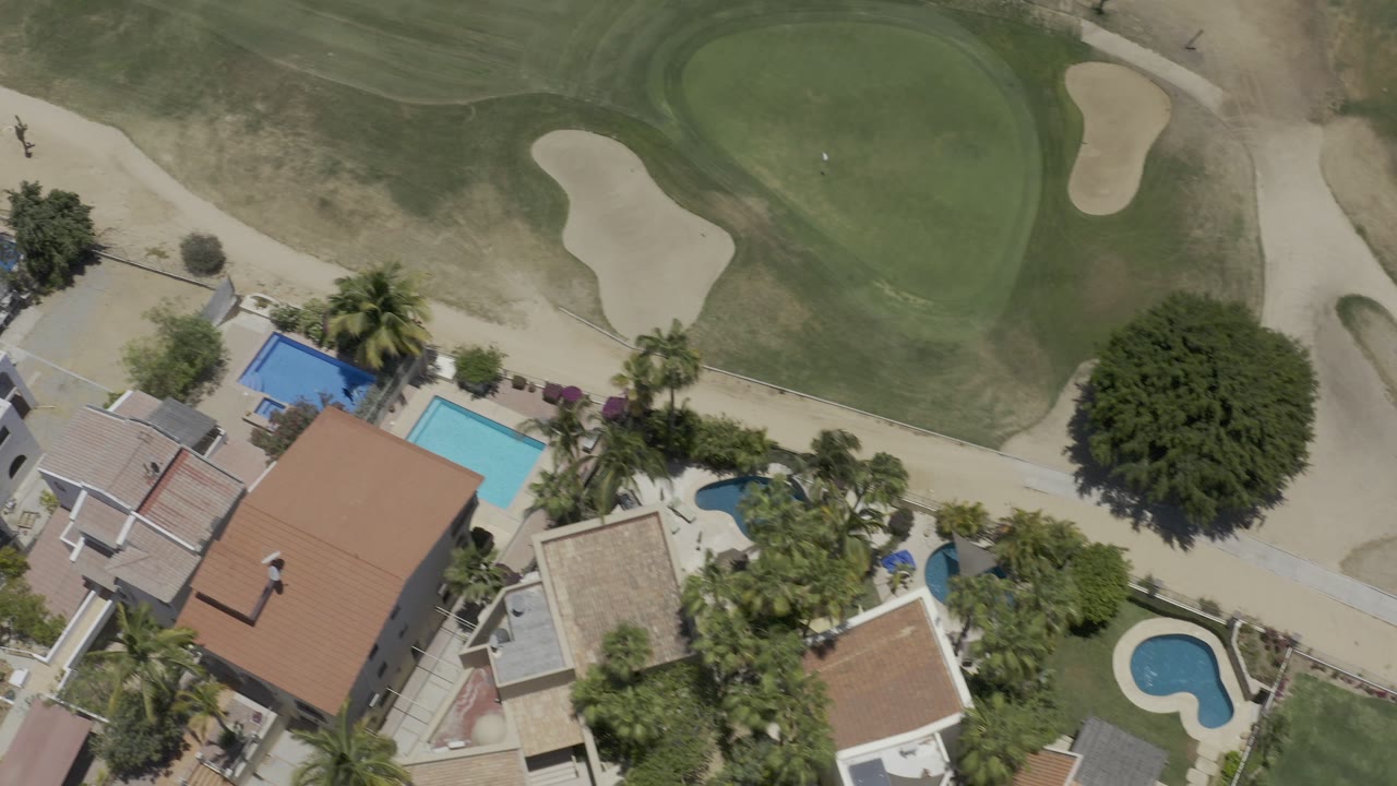 Overhead view of homes, pools, palms, and a golf green.