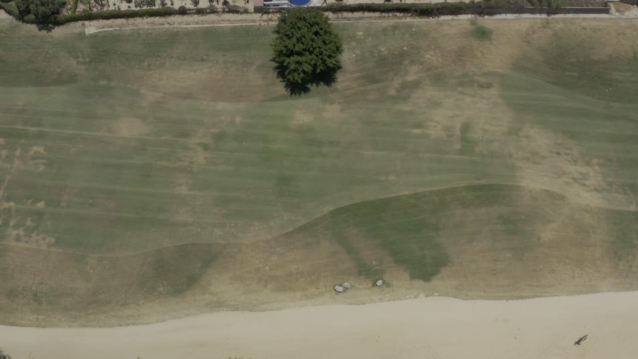 Overhead green field with dry patches, path, and resort edge.