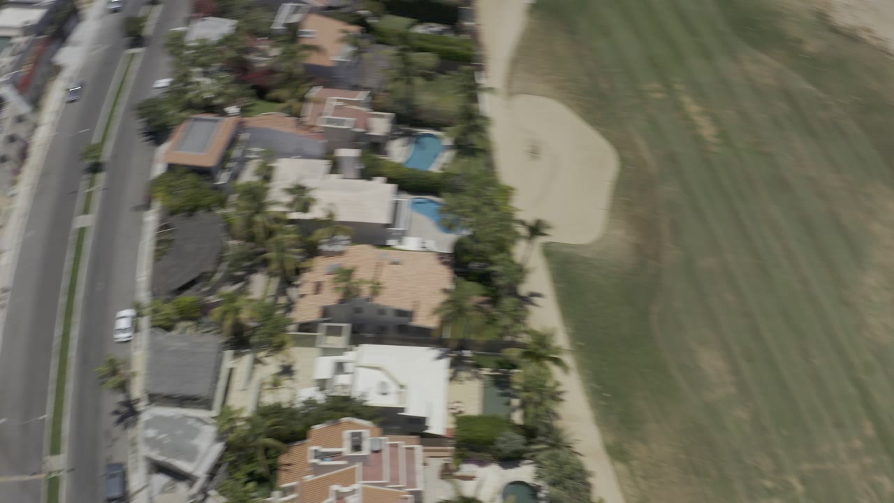 Overhead view of houses beside a green fairway and curved road.