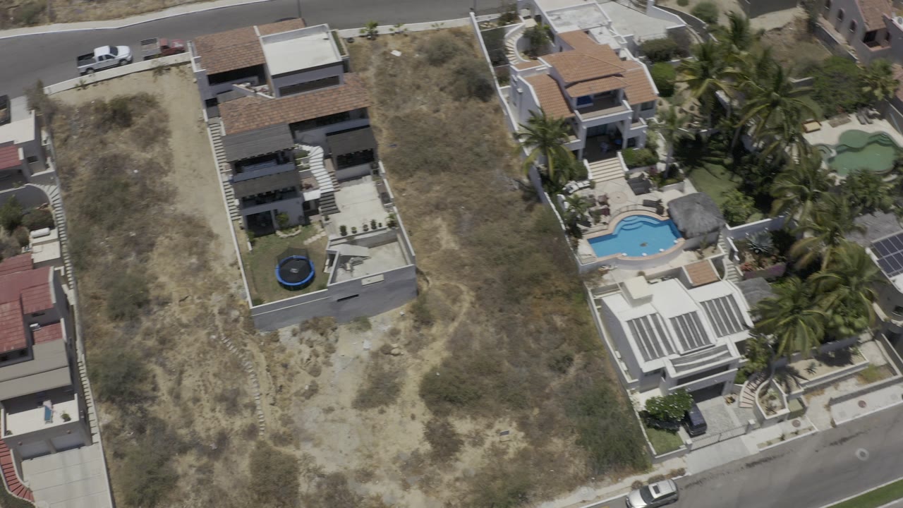 Aerial view of hillside homes, pools, palms, and a curving road.