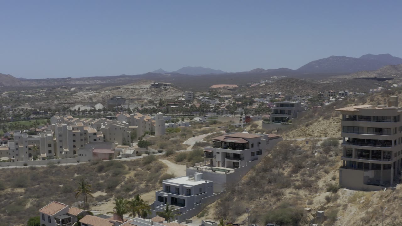 Aerial view of hillside homes and dry terrain below distant mountains.