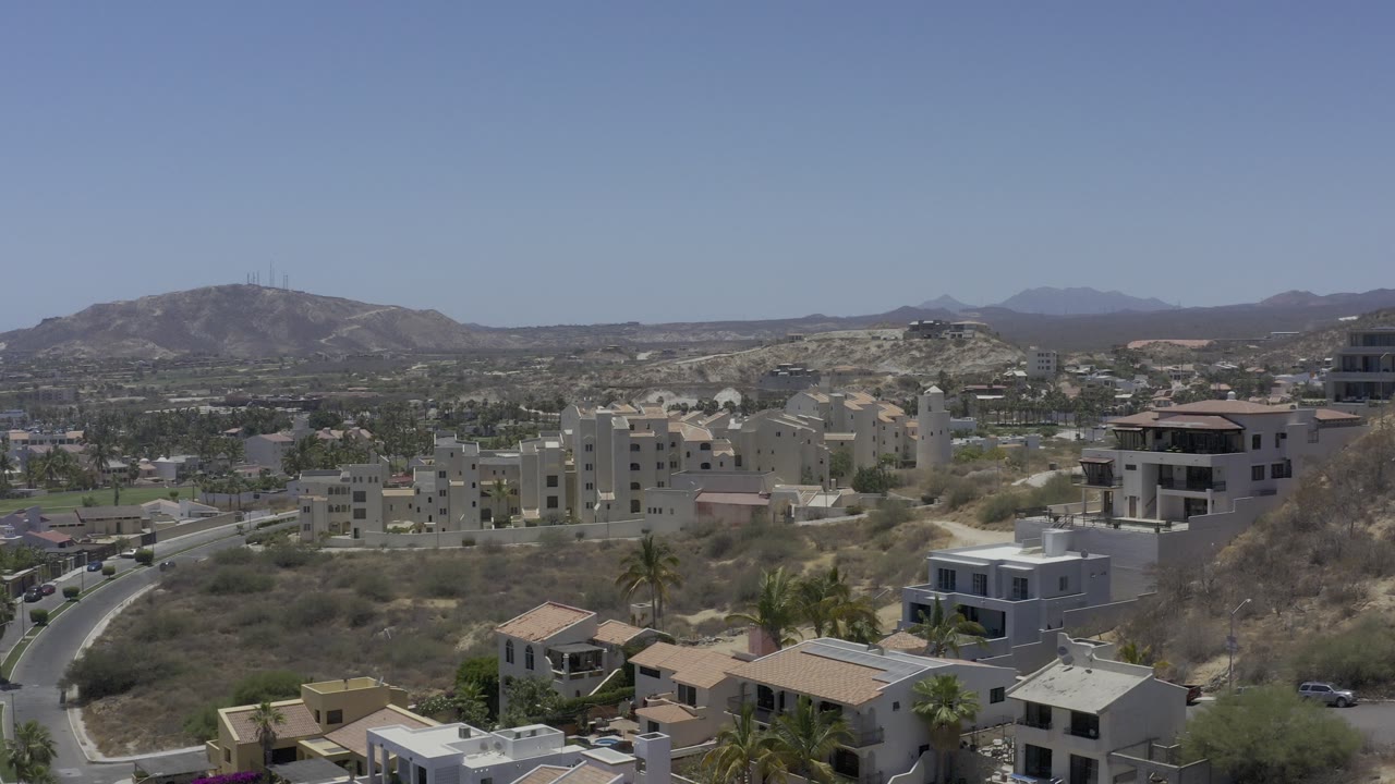 Aerial view over hillside homes and a valley town under a blue sky.