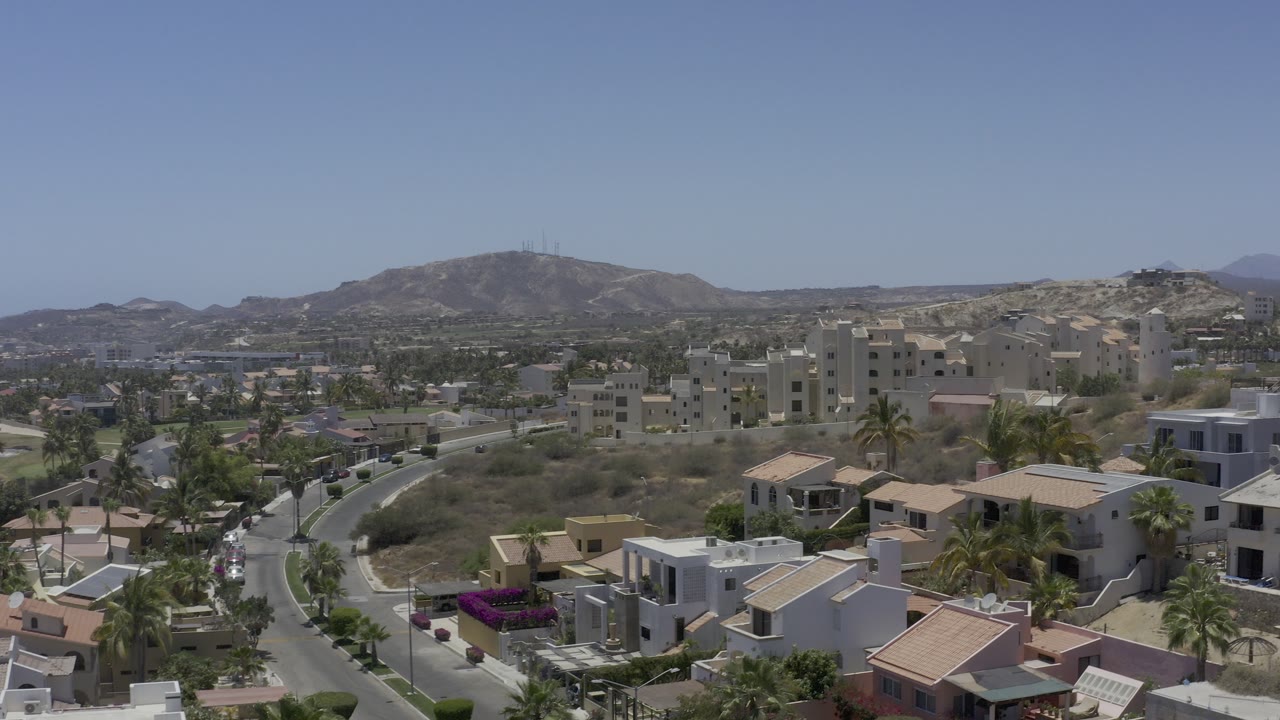 Elevated view over Los Cabos homes, roads, palms, and distant hills.