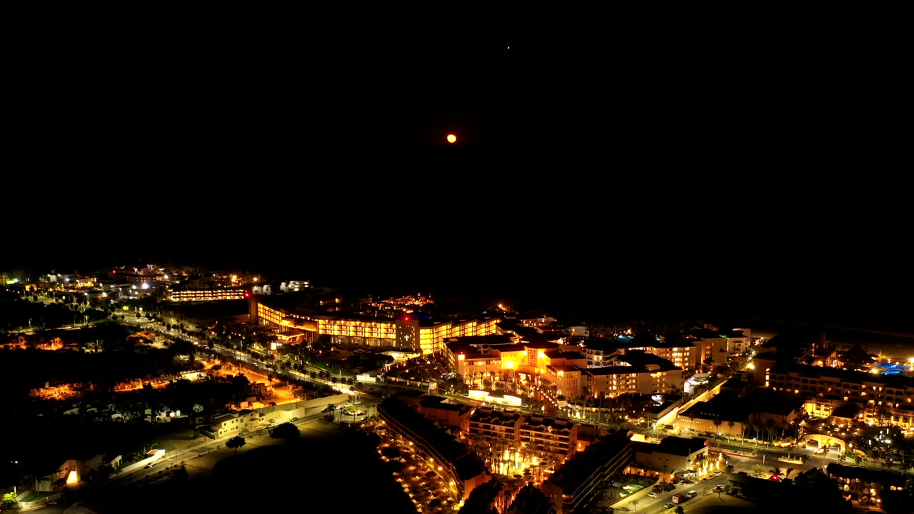 Night aerial view of bright coastal buildings under a dark sky