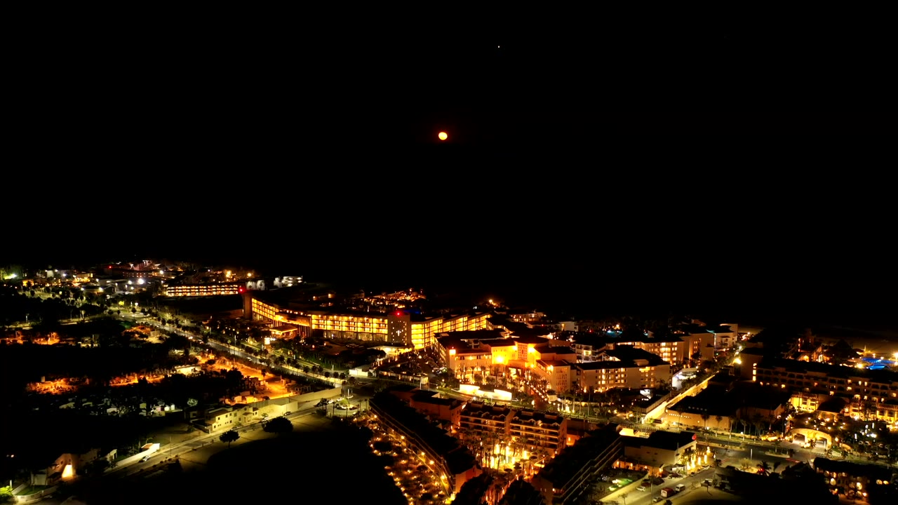 Los Cabos, Mexico appears from above at night, with bright road lines and warm building lights below a wide black sky and no visible people.