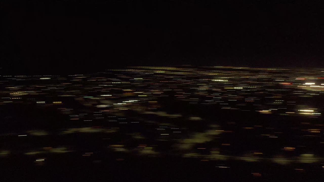 Los Cabos nighttime view with more defined rows of small yellow lights in the distance, dark land in the foreground, and no visible people.